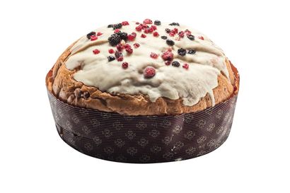 Una torta panettone rotonda, ricoperta di glassa chiara e decorata con frutti di bosco secchi, in uno stampo di carta marrone.