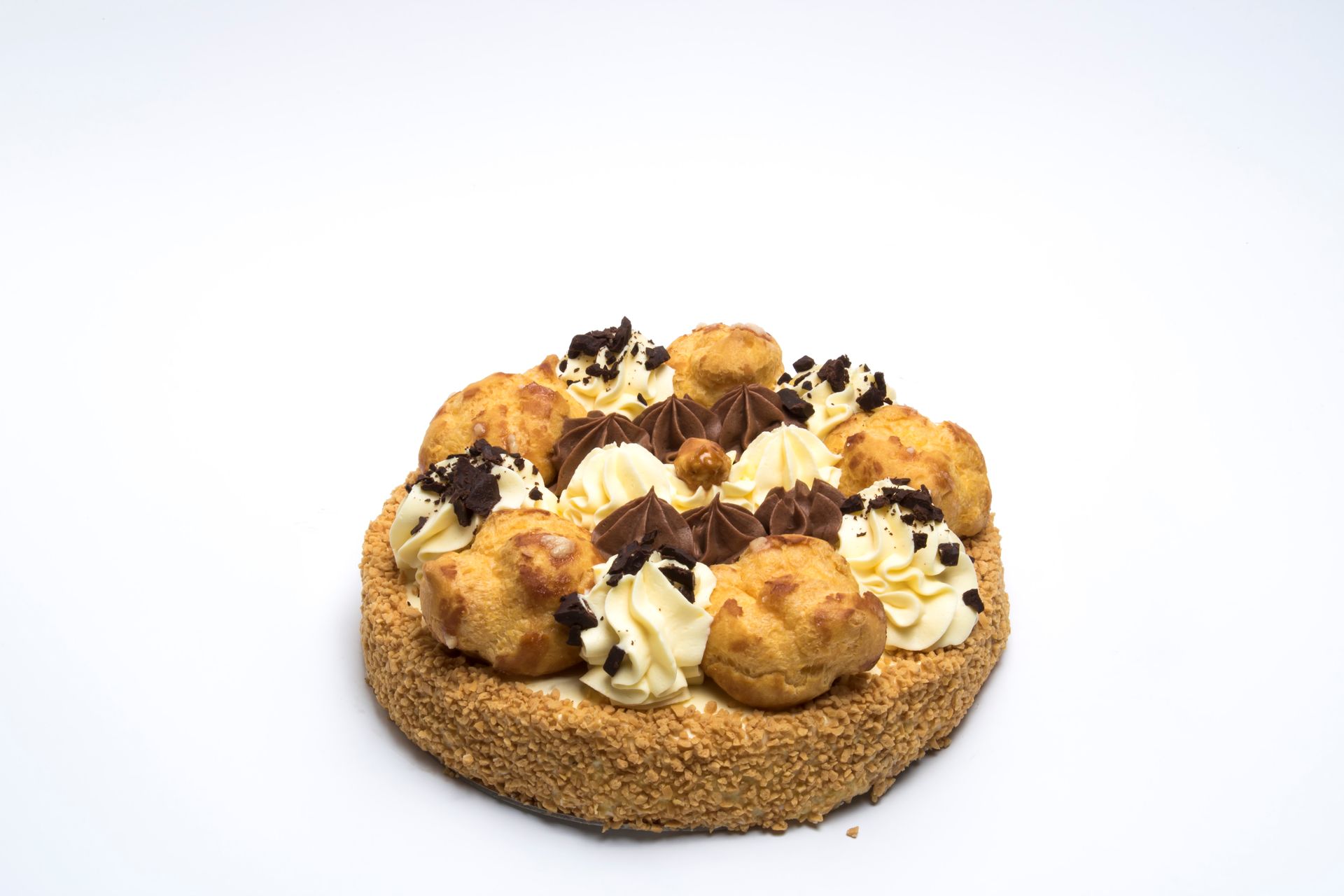 Una crostata rotonda decorata con bignè, glassa alla vaniglia montata, gocce di cioccolato fondente e granella di cacao su uno sfondo bianco.