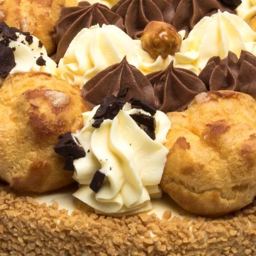 Una torta sontuosa guarnita con bignè, spirali di glassa al cioccolato e alla vaniglia e una crosta croccante ricoperta di noci.