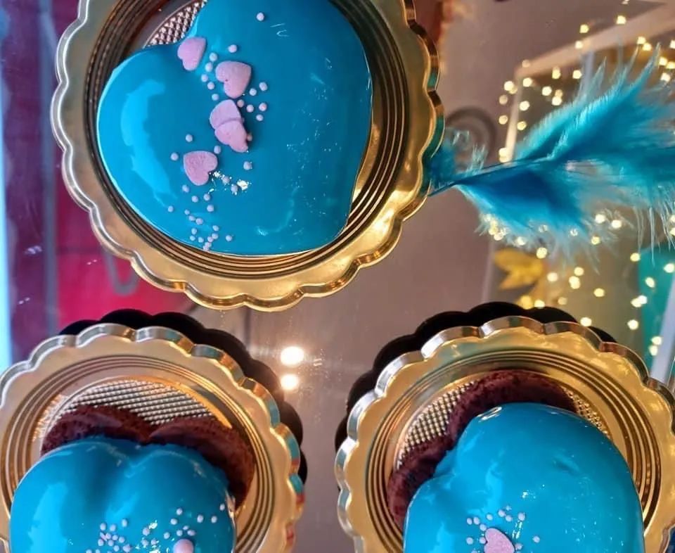 Tre torte a forma di cuore glassate di un blu acceso, decorate con minuscoli cuoricini rosa, su vassoi per torte dorati con bordi smerlati.