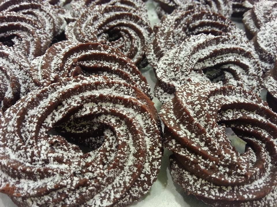 Primo piano di alcuni biscotti al cioccolato fondente, decorati con una sac à poche a forma di spirale e spolverati di zucchero a velo.