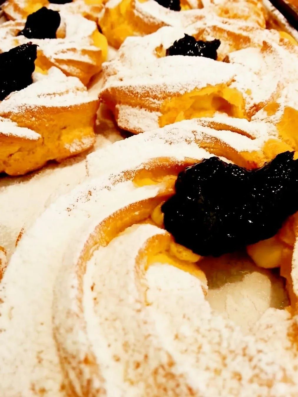 Primo piano di bignè rotondi spolverati di zucchero a velo e guarniti con frutta scura.