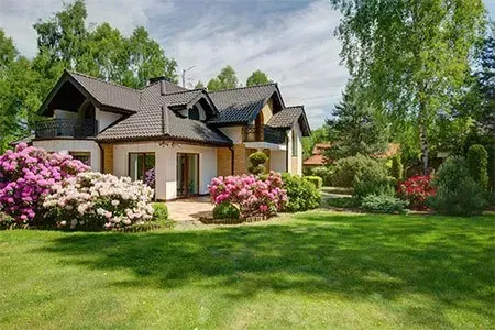 A large house with a lush green lawn and flowers in front of it.