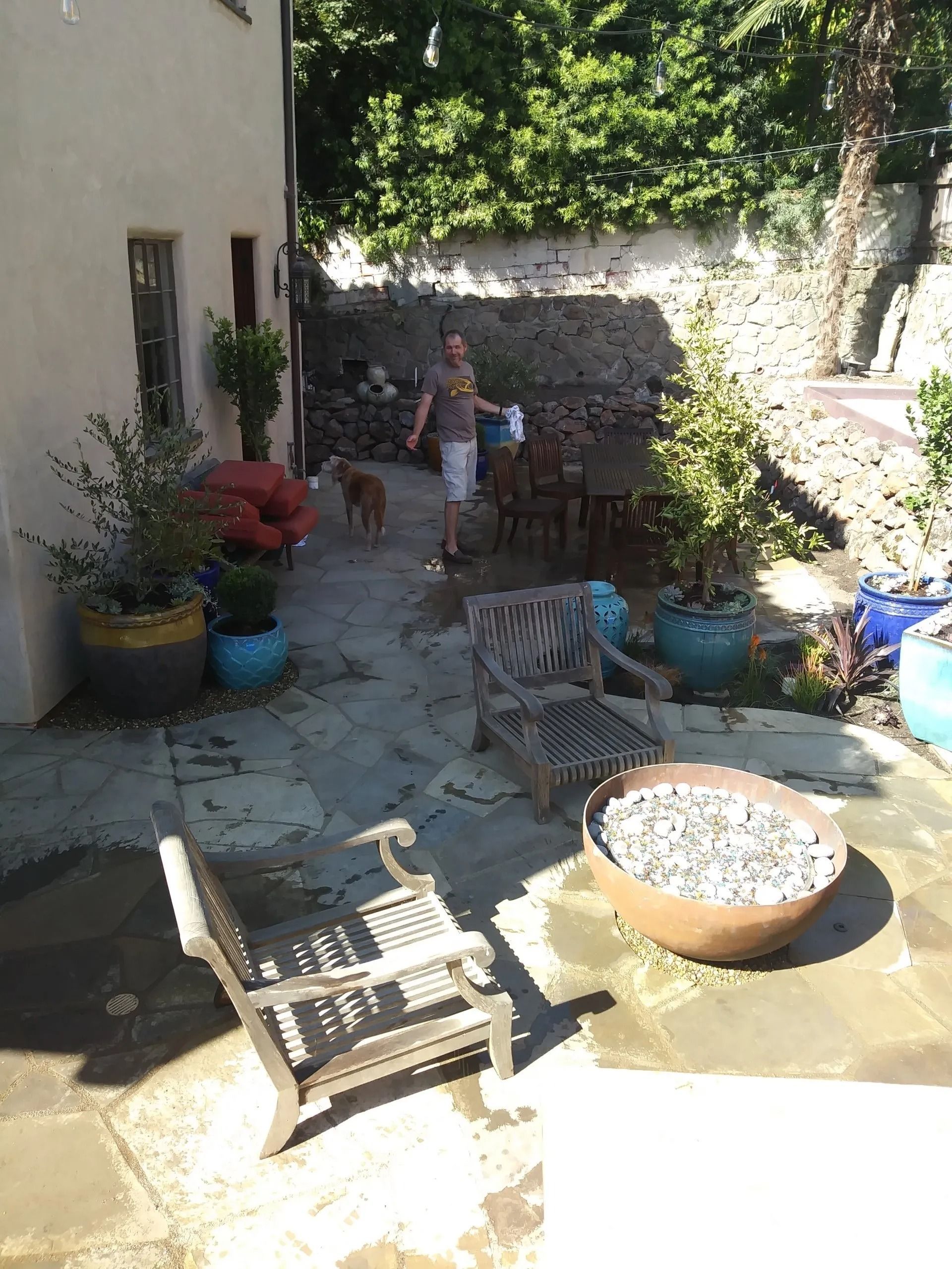A man is walking a dog on a patio with chairs and a fire pit.