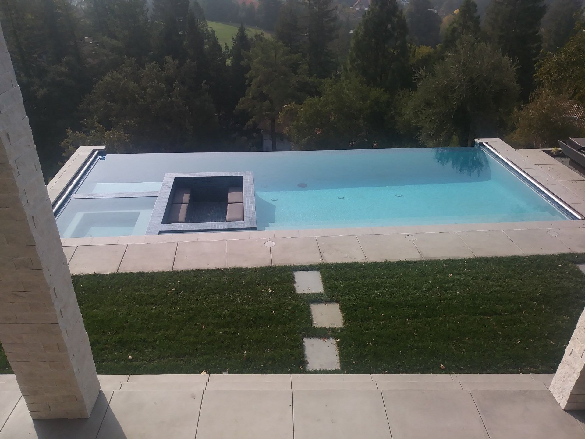 A large swimming pool is surrounded by grass and trees