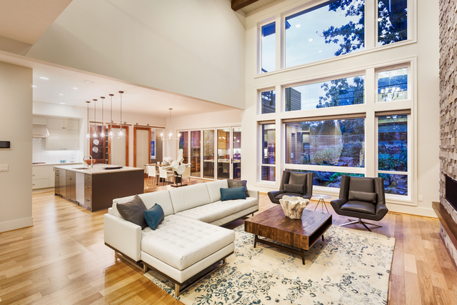 Bright modern living room with tall windows, white sectional sofa, armchairs, and hardwood floors