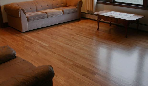 Empty living room with hardwood floors, a beige sofa, coffee table, and large window light