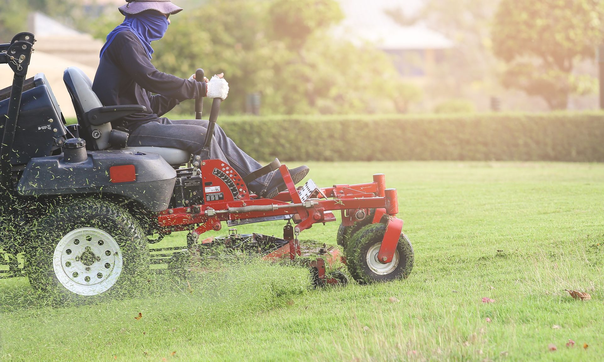 Man on a red zero-turn mower cutting grass in a sunny field.