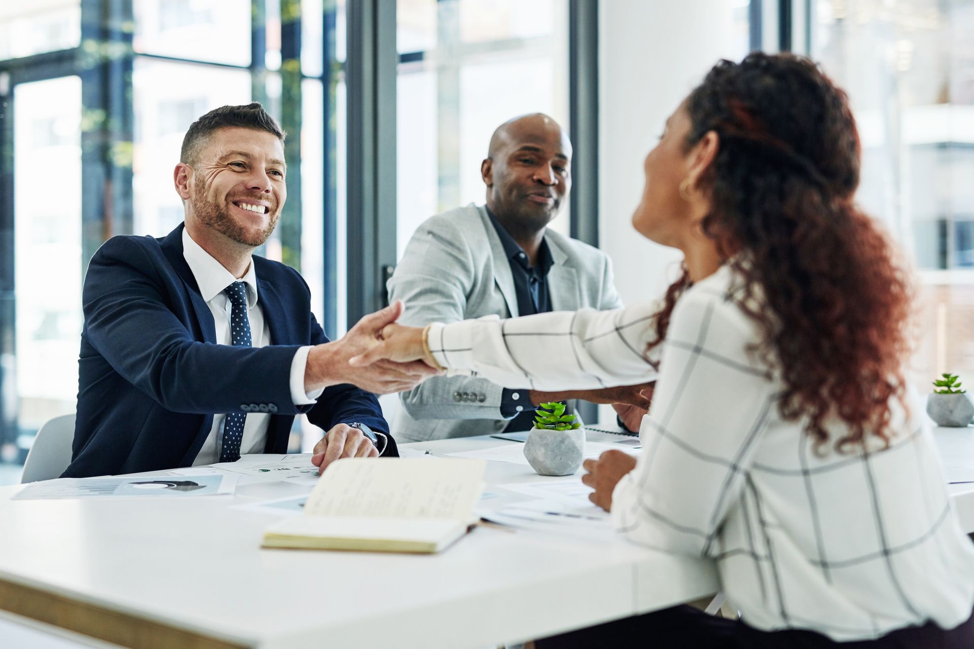 A man and a woman are shaking hands while sitting at a table.