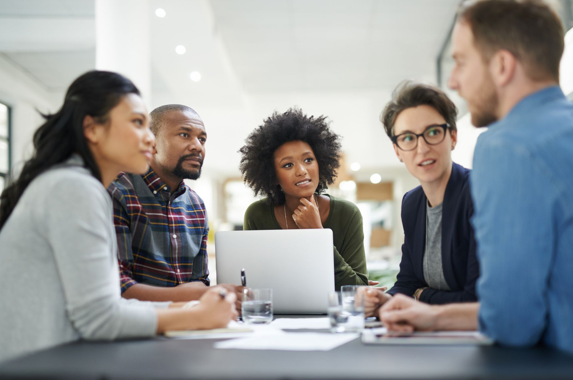 A group of people are sitting around a table looking at a laptop.