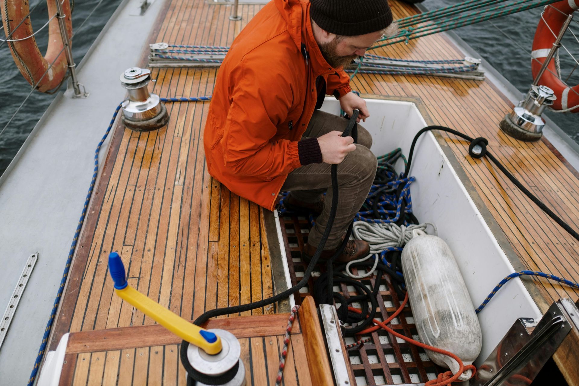 A man in an orange jacket is sitting on the deck of a boat.