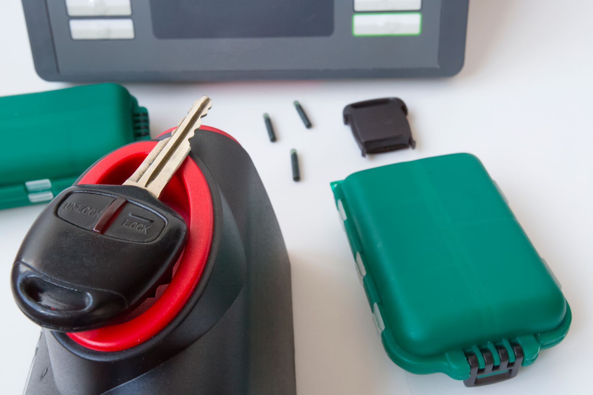 Car key inside a black and red device, with green cases, and small black transponder chips on a white surface.