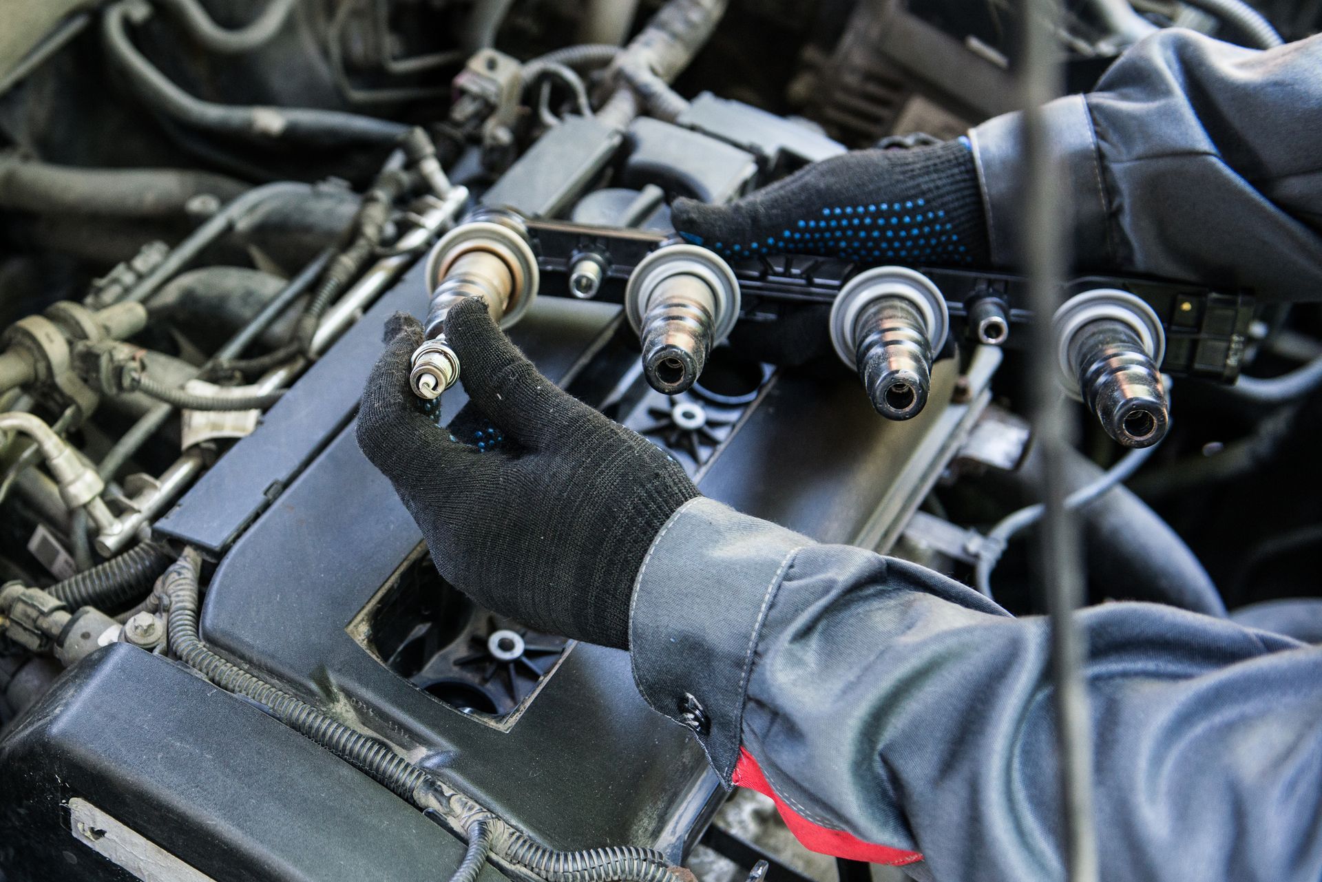 Hands in black gloves installing a spark plug in a car engine compartment.