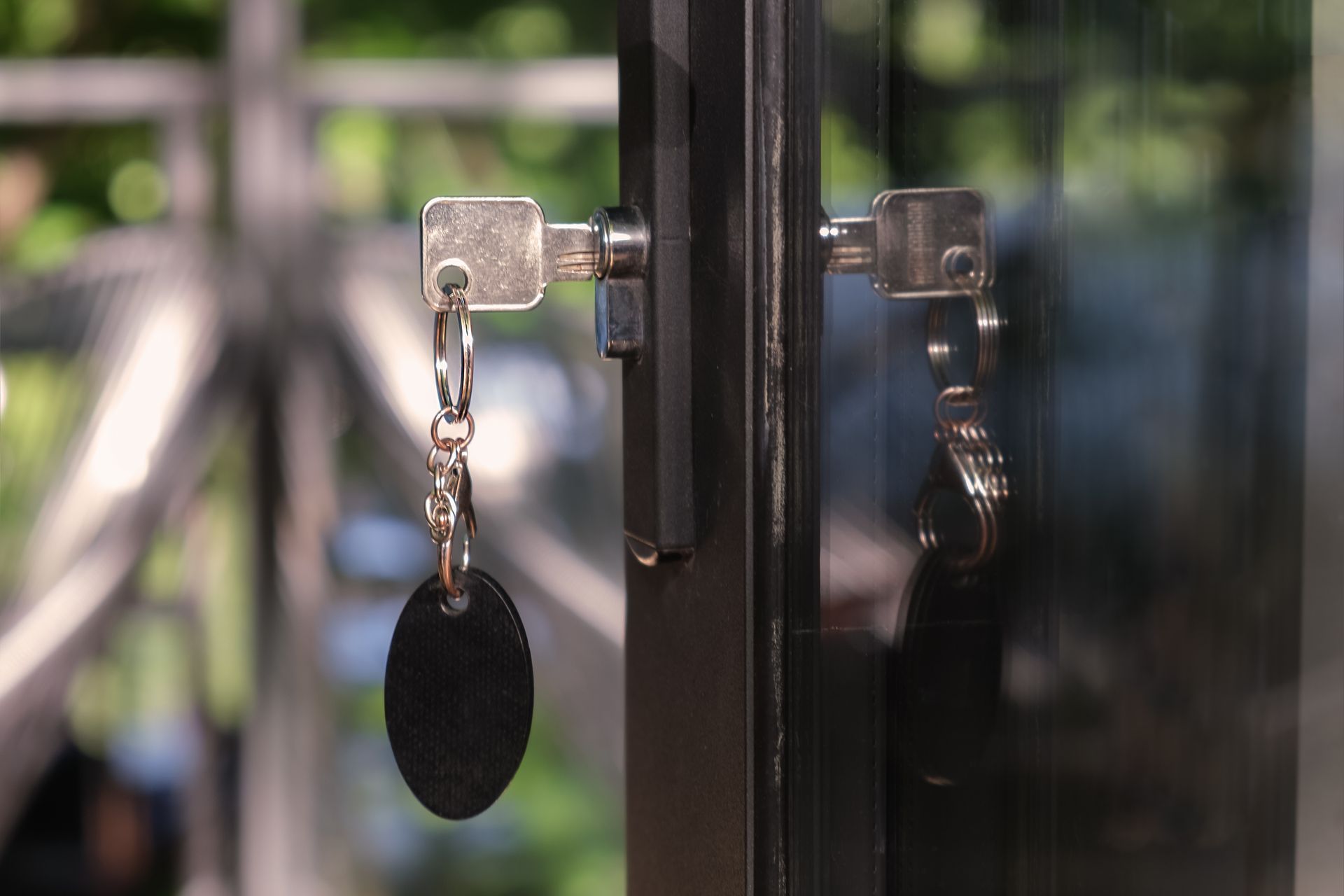 Keys in door lock on a glass door. One key hangs with a black tag.