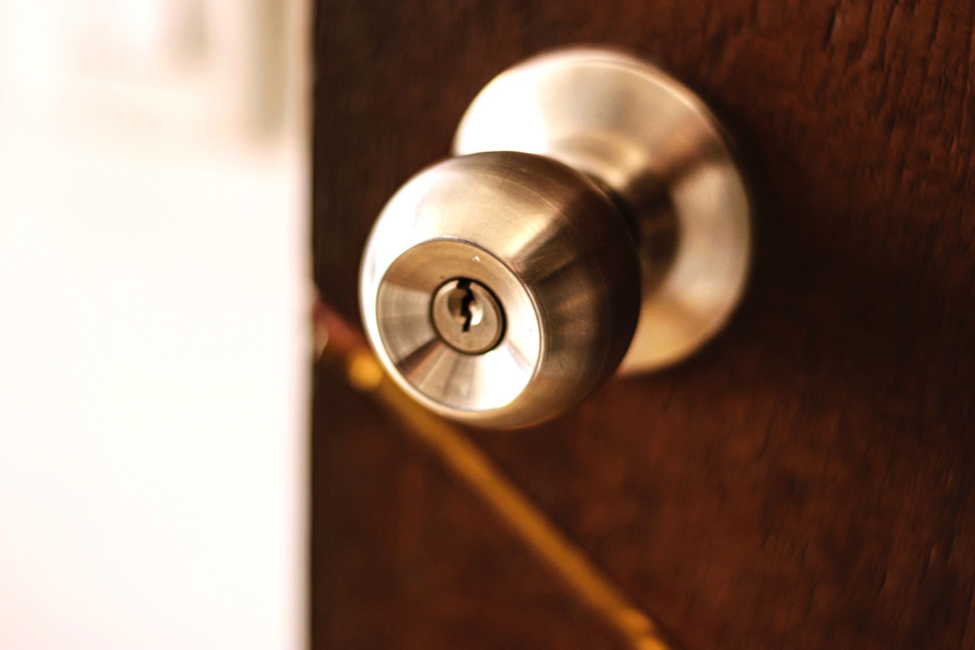 Silver doorknob with a keyhole on a dark brown wooden door.