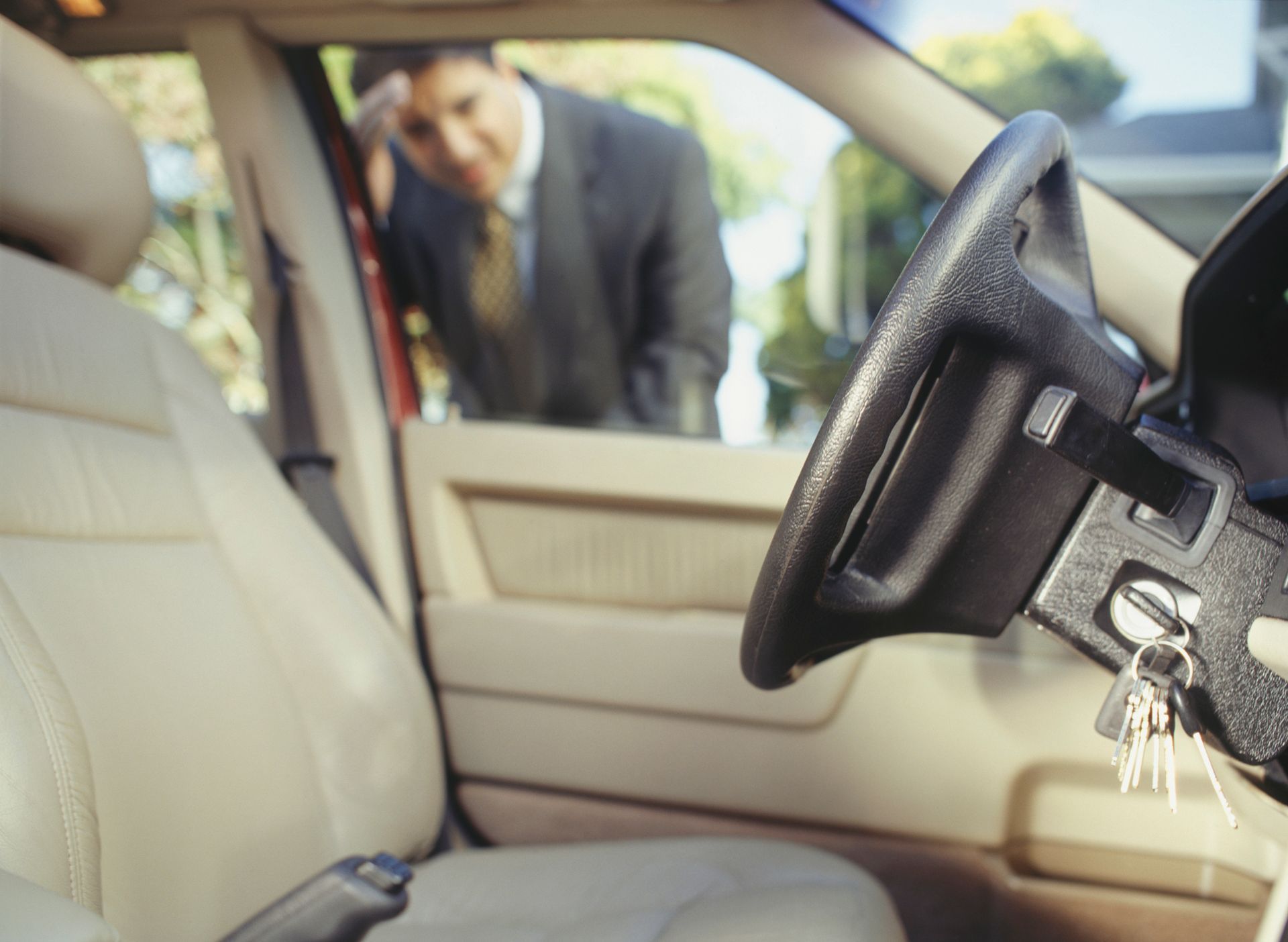 Man locked out of car, looking frustrated; keys in ignition, steering wheel in foreground.