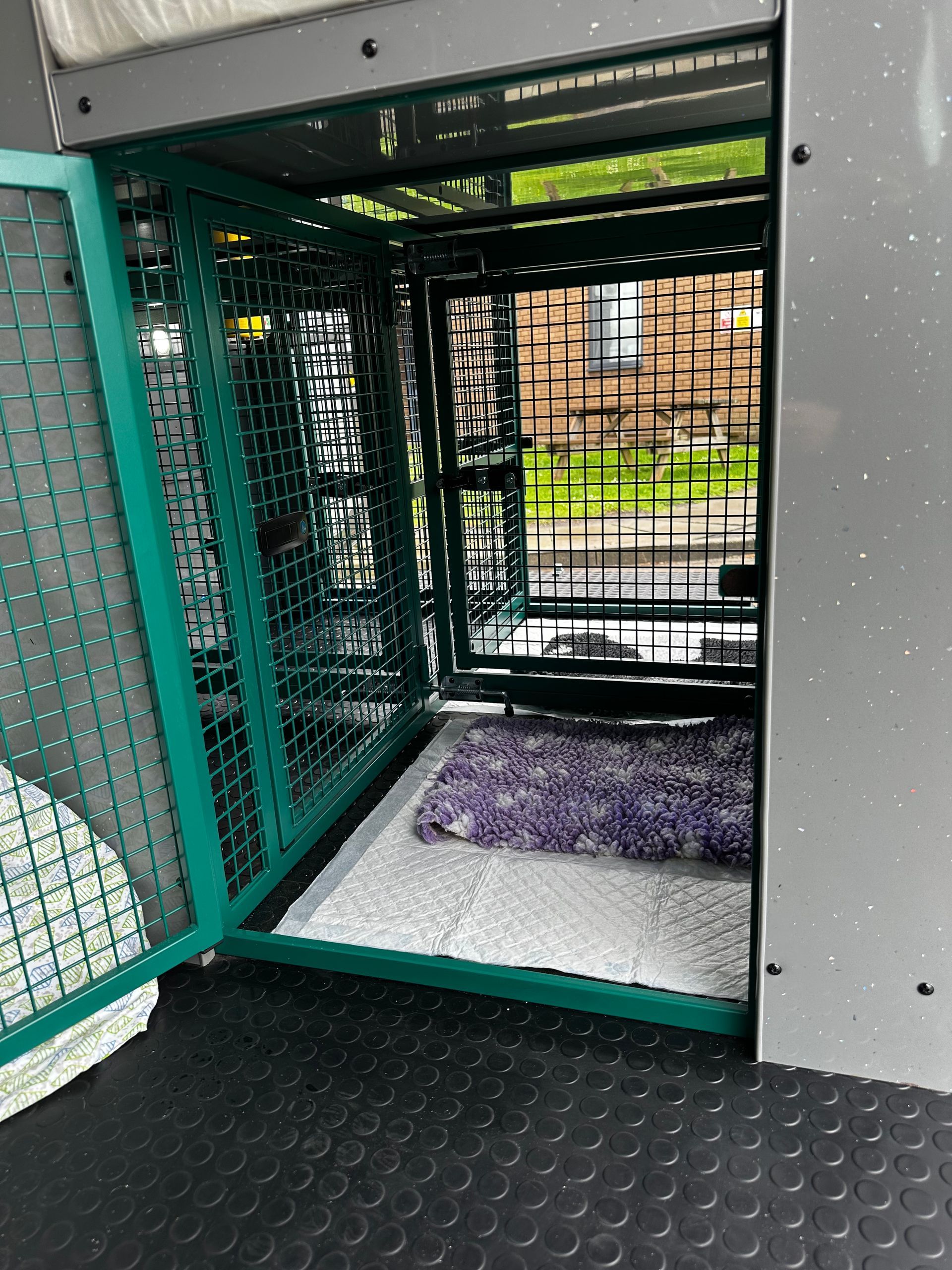 Green metal dog crate inside a vehicle, with a purple bed and a pad on the floor.