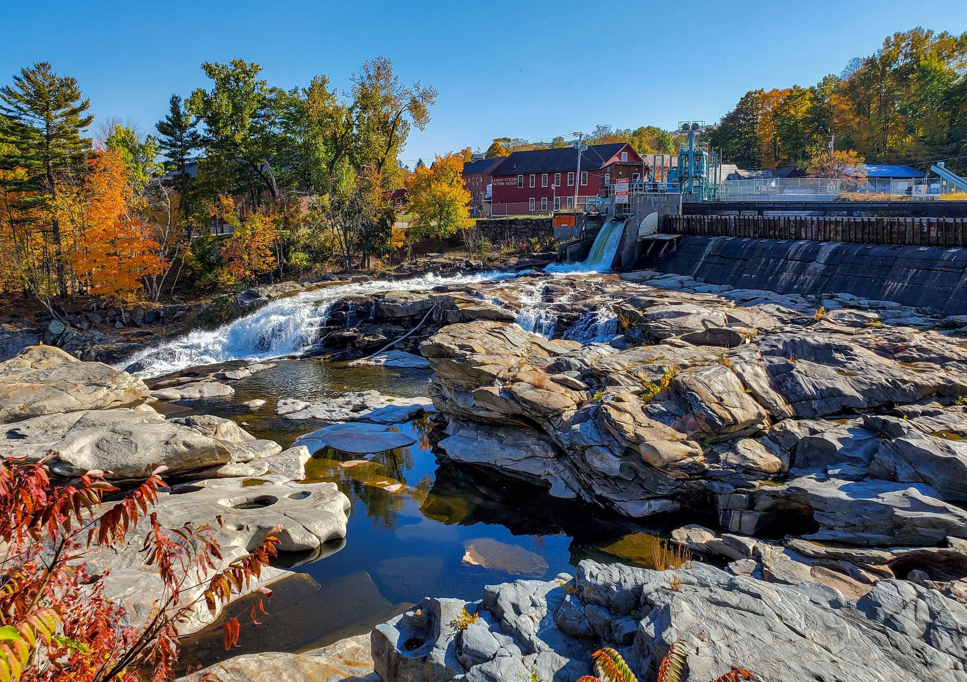 Rocky river with waterfall, red building in the background, fall foliage.