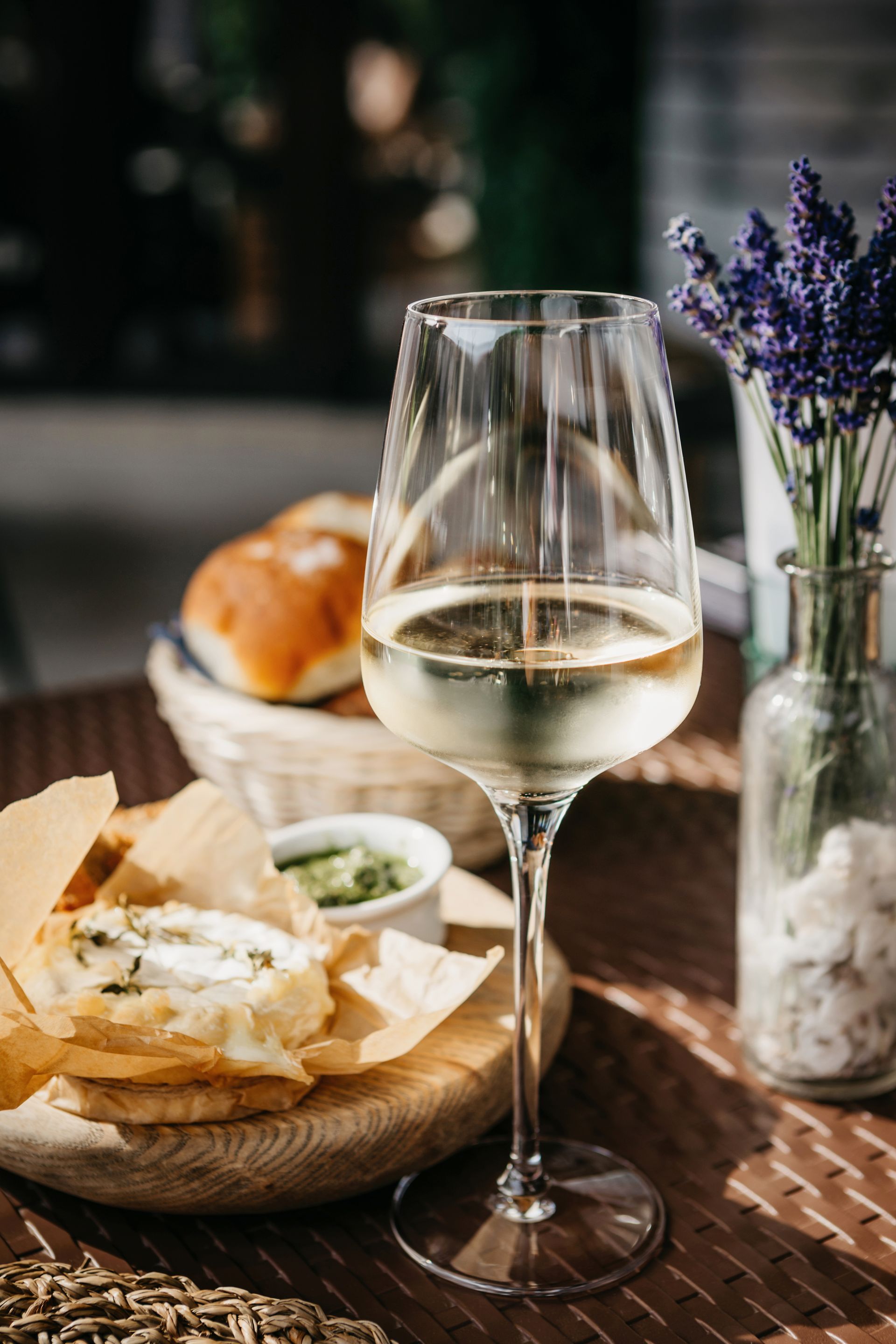 Wine glass with white wine, bread, small tart, and lavender on a table.