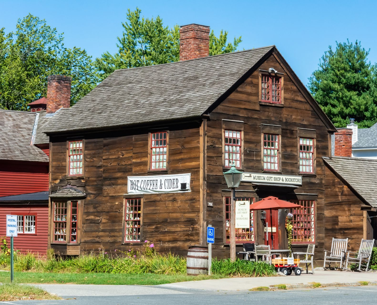 A historic, weathered wooden building featuring a gabled roof and multi-pane windows, with a small outdoor cafe area in front.