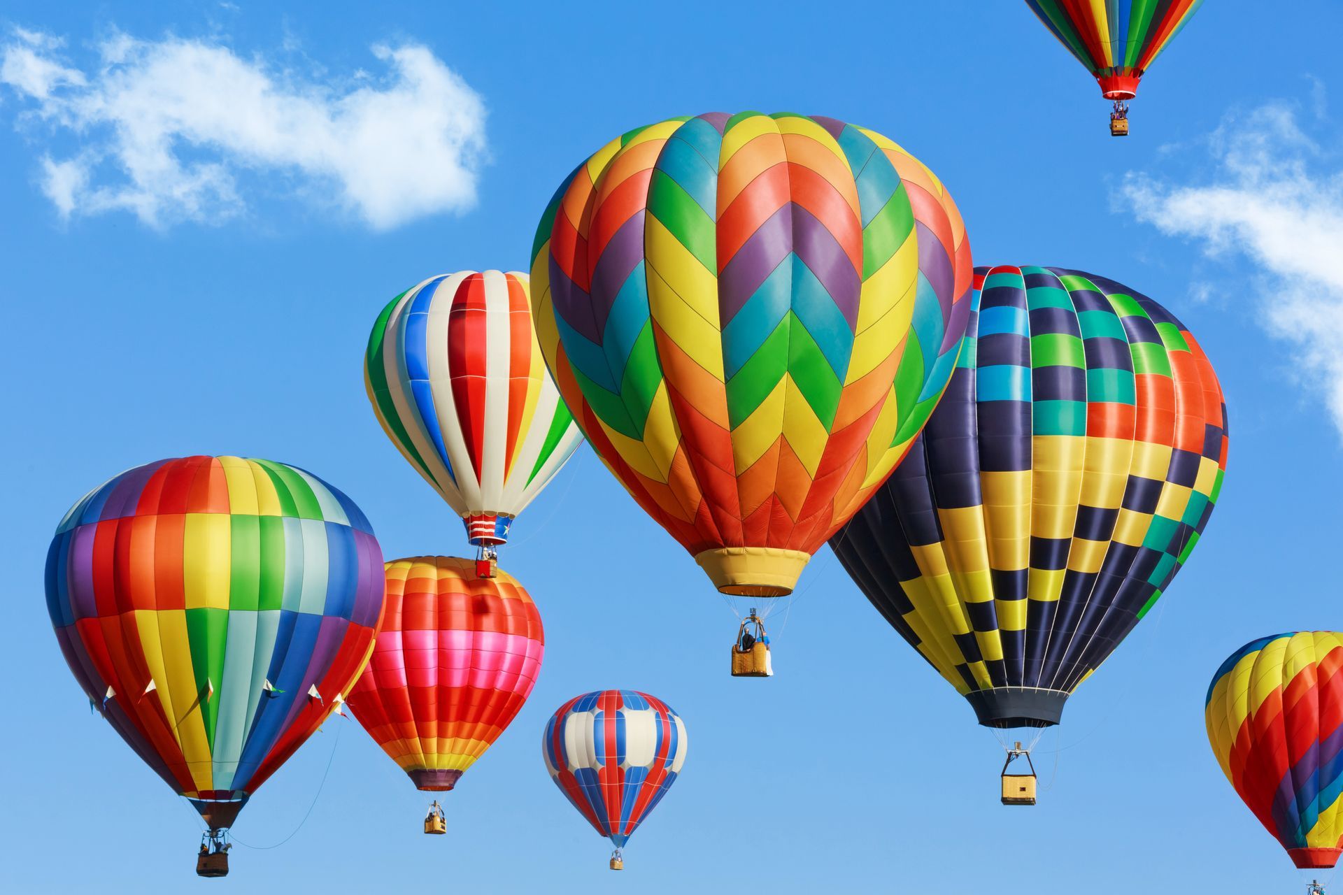Colorful hot air balloons against a blue sky with fluffy clouds.
