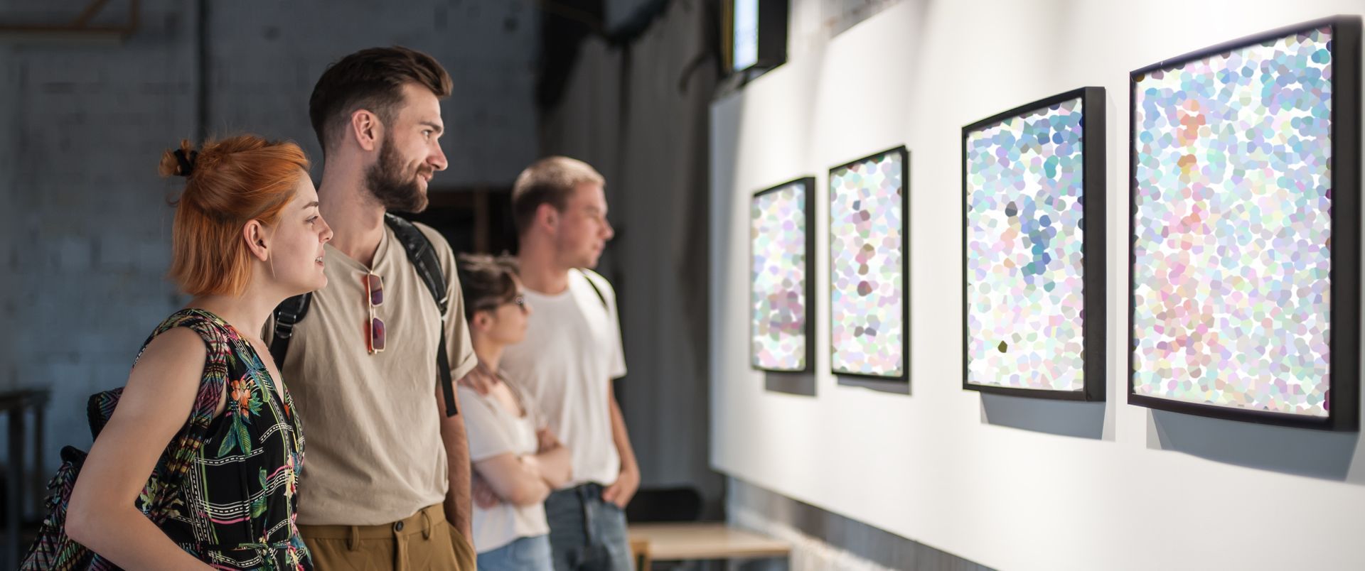 Four people looking at art in a gallery. The artwork is framed and hung on a white wall.