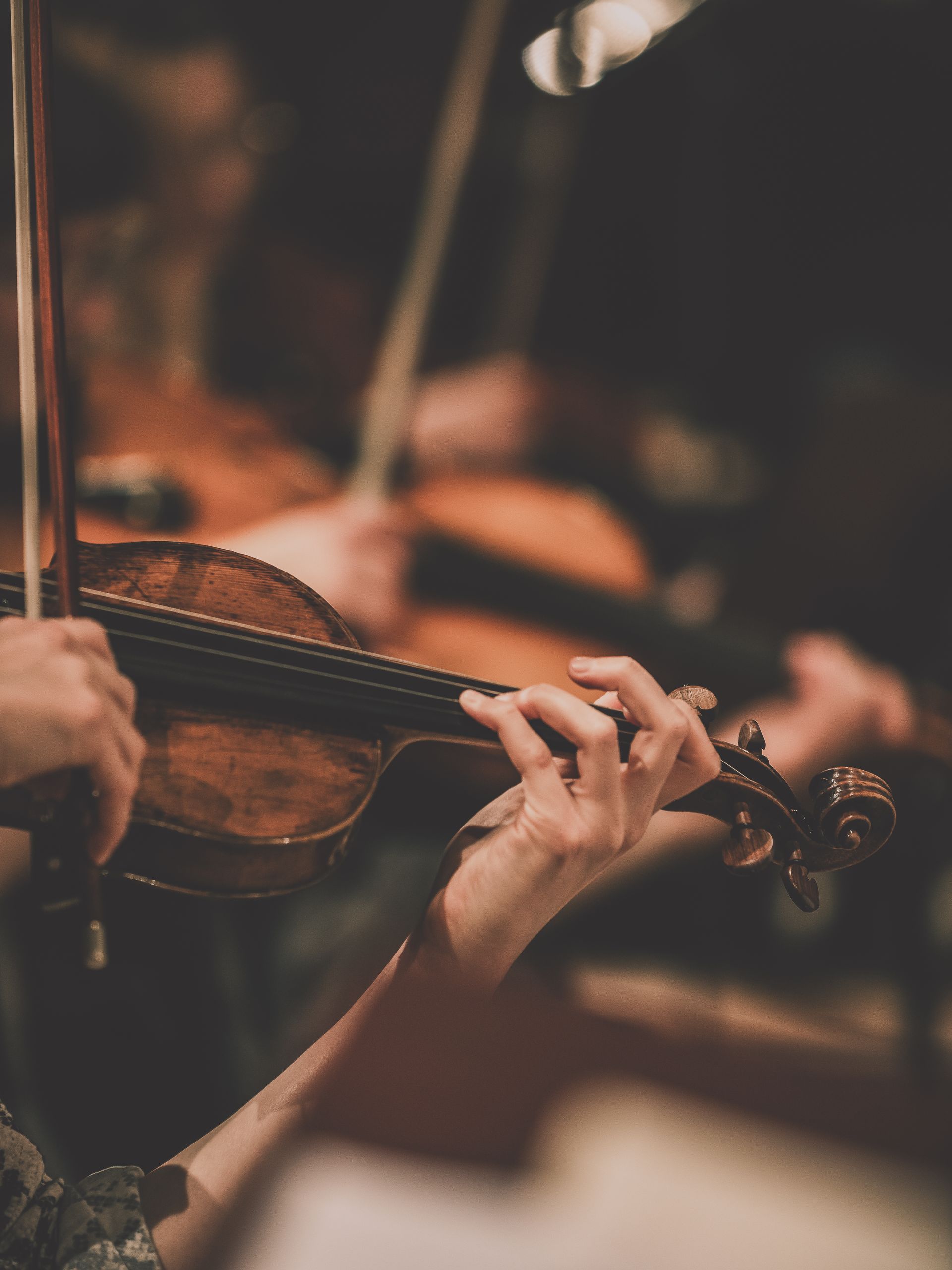Person playing a violin with a bow in an orchestra; close up.