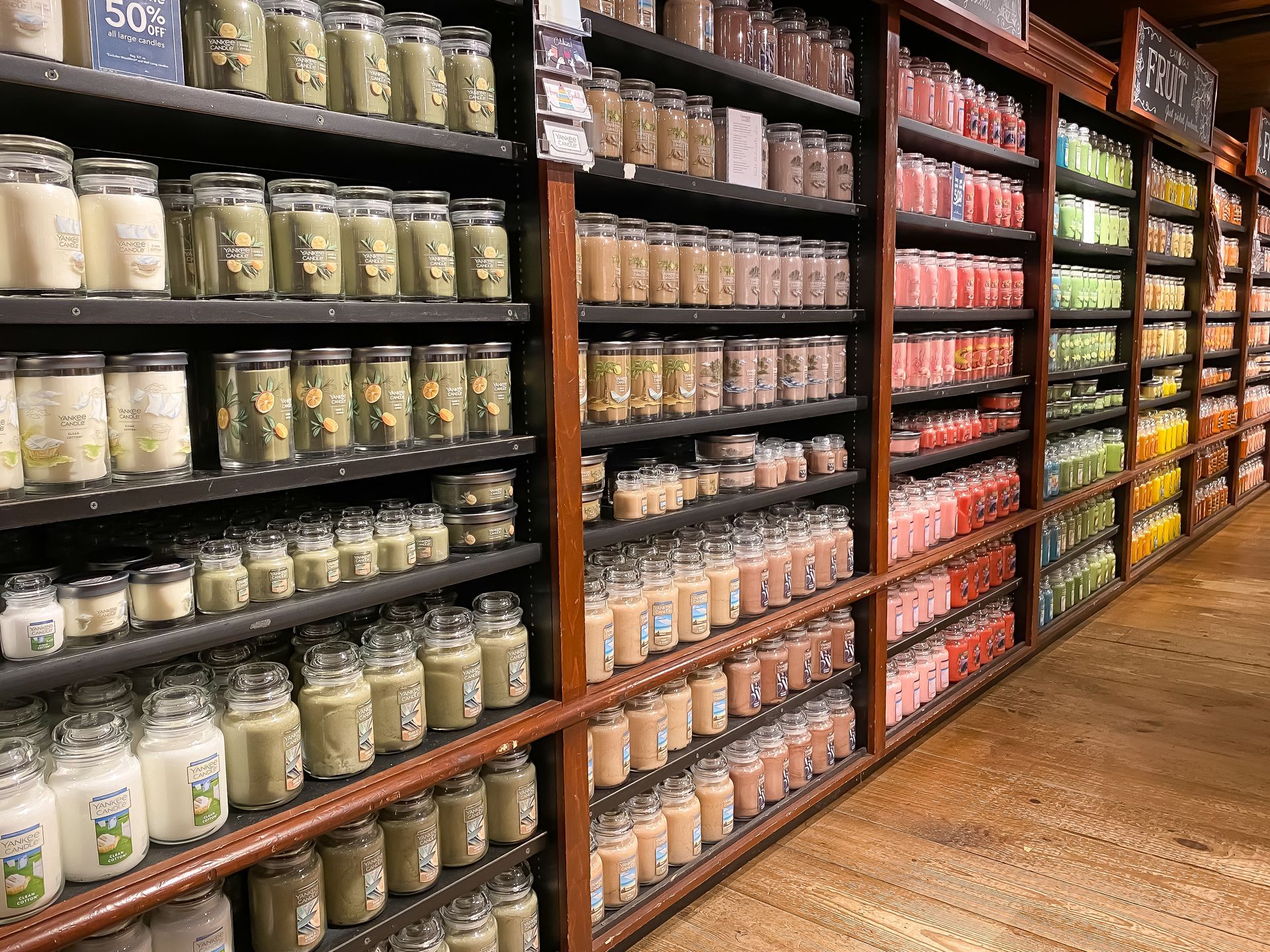 Shelves filled with numerous rows of jarred candles in a variety of colors arranged in a retail store setting.