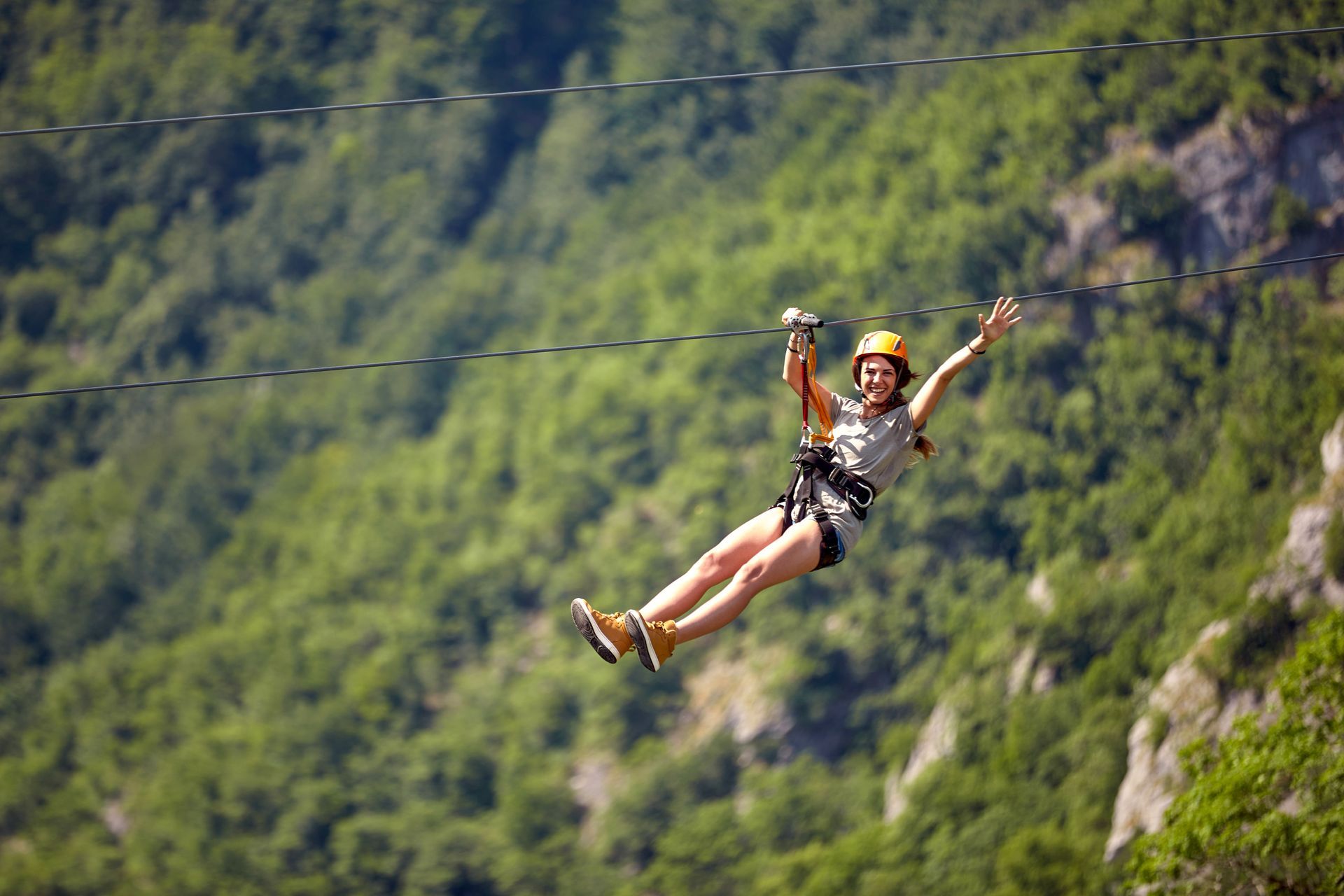 Person ziplining over a forested mountain valley, arms raised in a harness