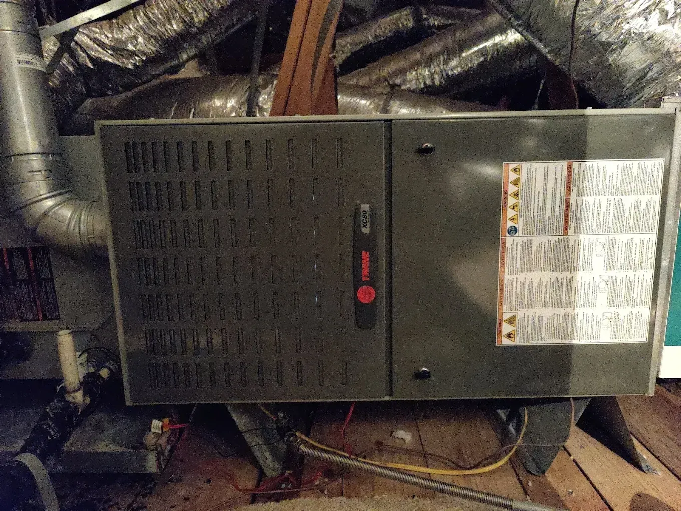Dark-colored Trane furnace in an attic. Ductwork and wood beams are visible in the background.