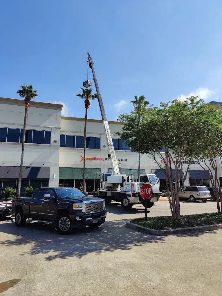 A large crane next to a white building with palm trees. A pickup truck is in front.
