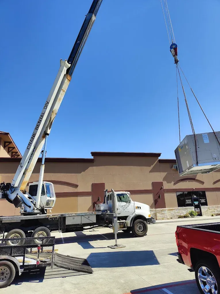 A crane lifting a large, round object near a commercial building on a sunny day.