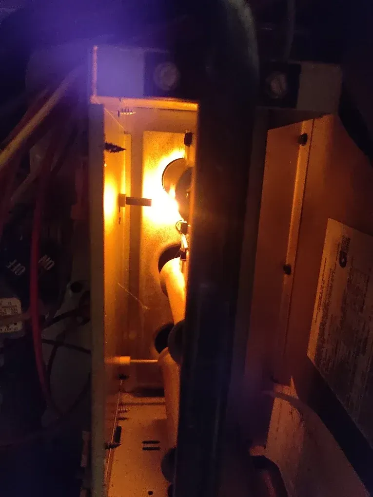 A furnace interior glows with a bright orange flame. Black pipes and metal components are visible inside.