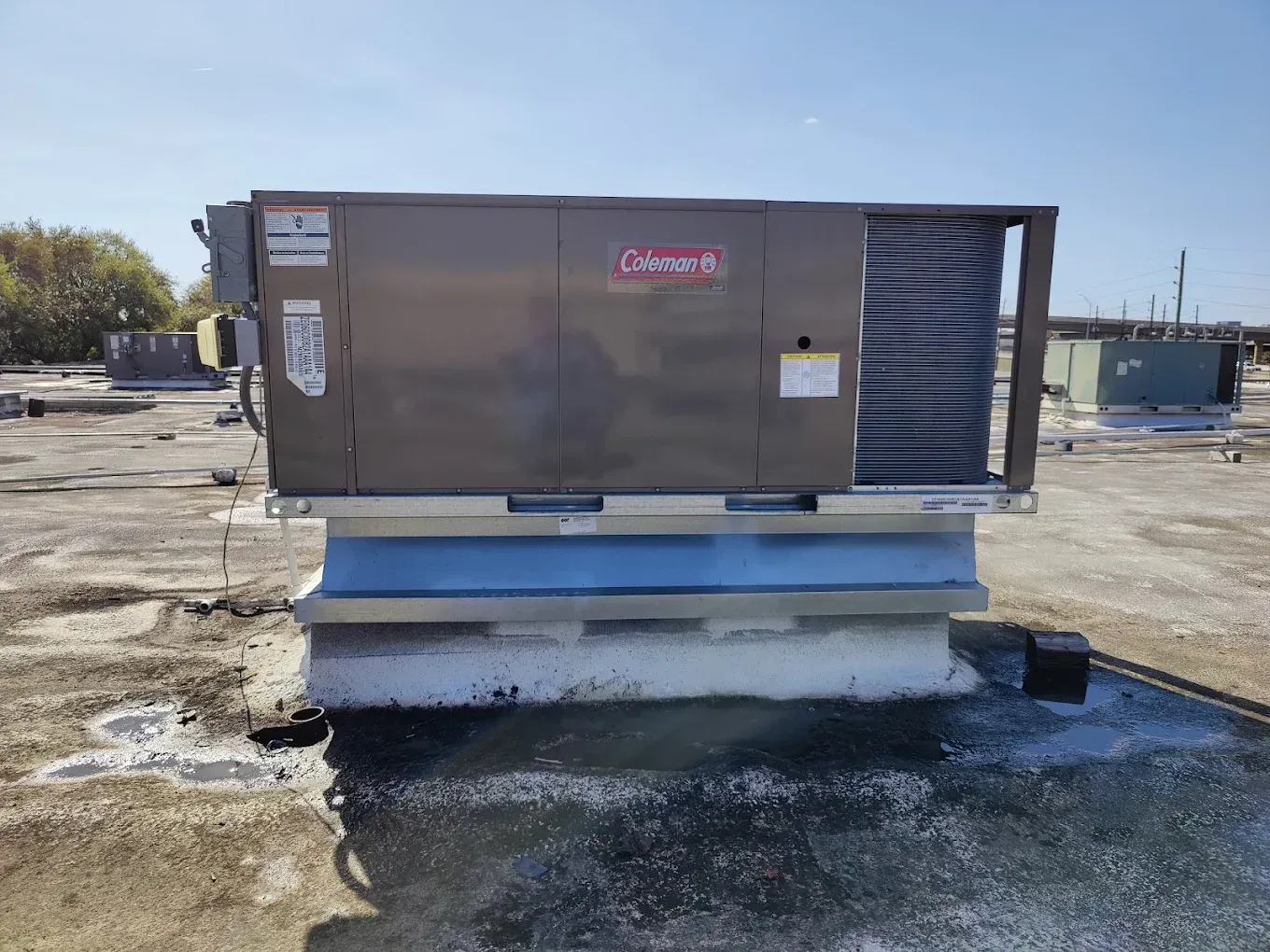 Coleman rooftop HVAC unit on a building with a blue and beige support.