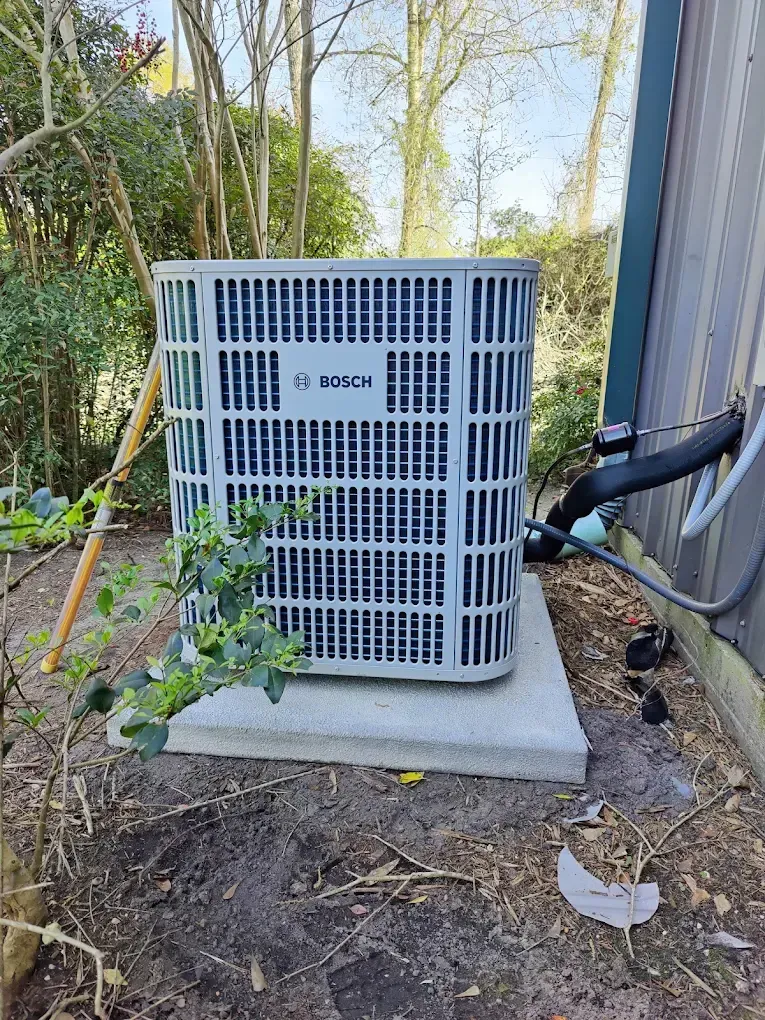 Bosch air conditioner unit on a concrete pad next to a building, outdoors.