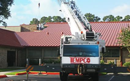 White crane lifting onto a red roof of a brick building; 