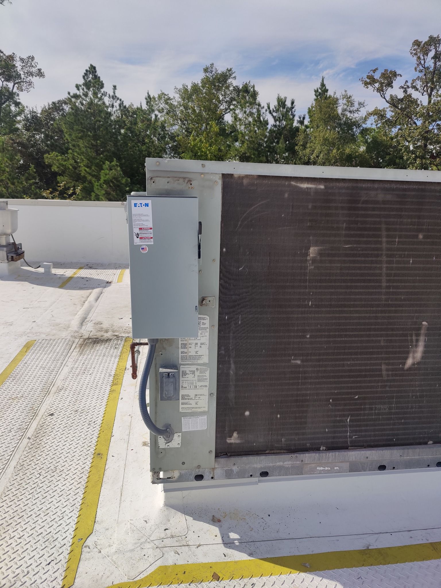 HVAC unit on a rooftop. Gray metal box attached to a coil. White roof with yellow safety stripes.