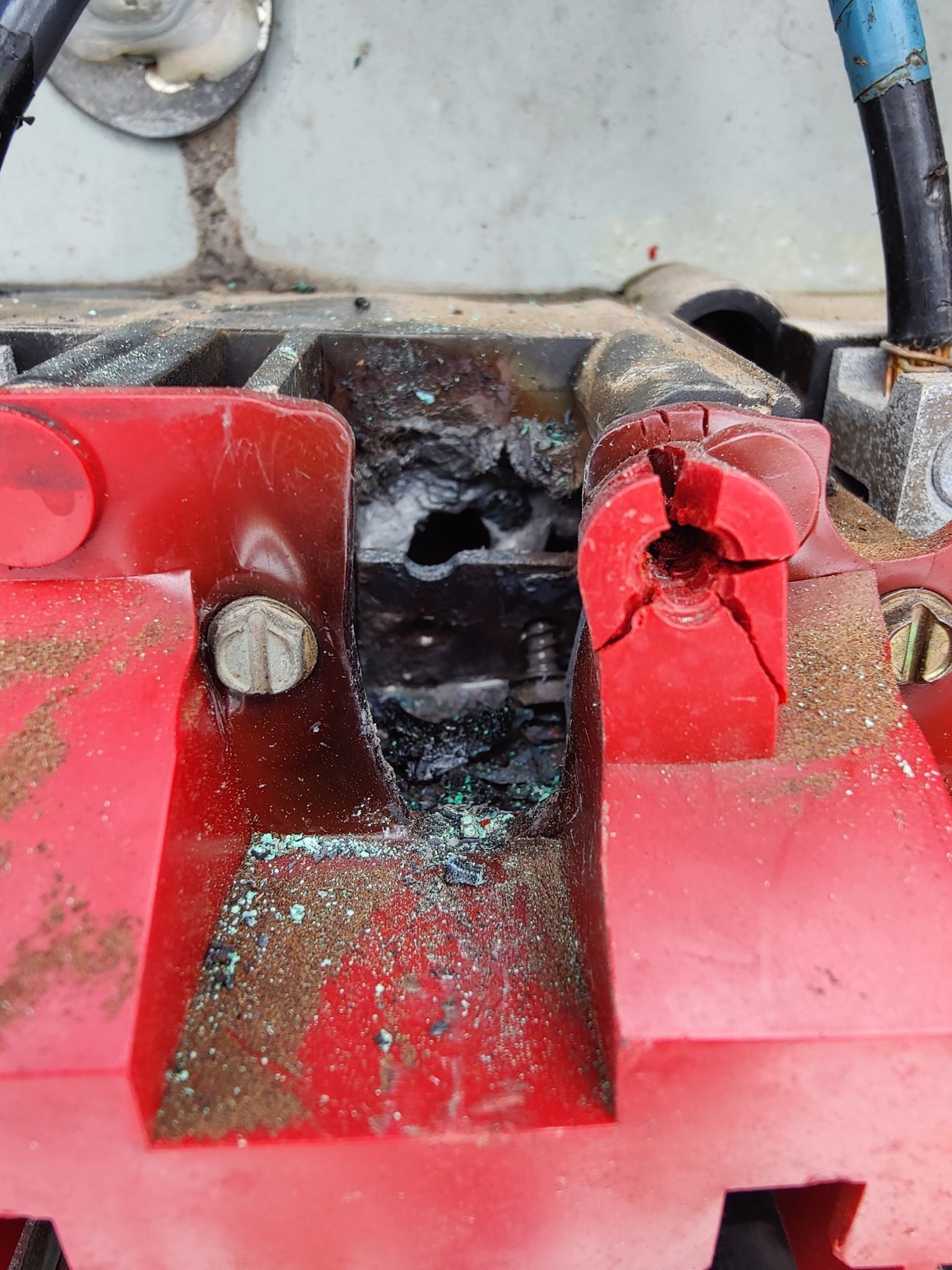 Damaged red electrical component with melted areas, crack, and corrosion.