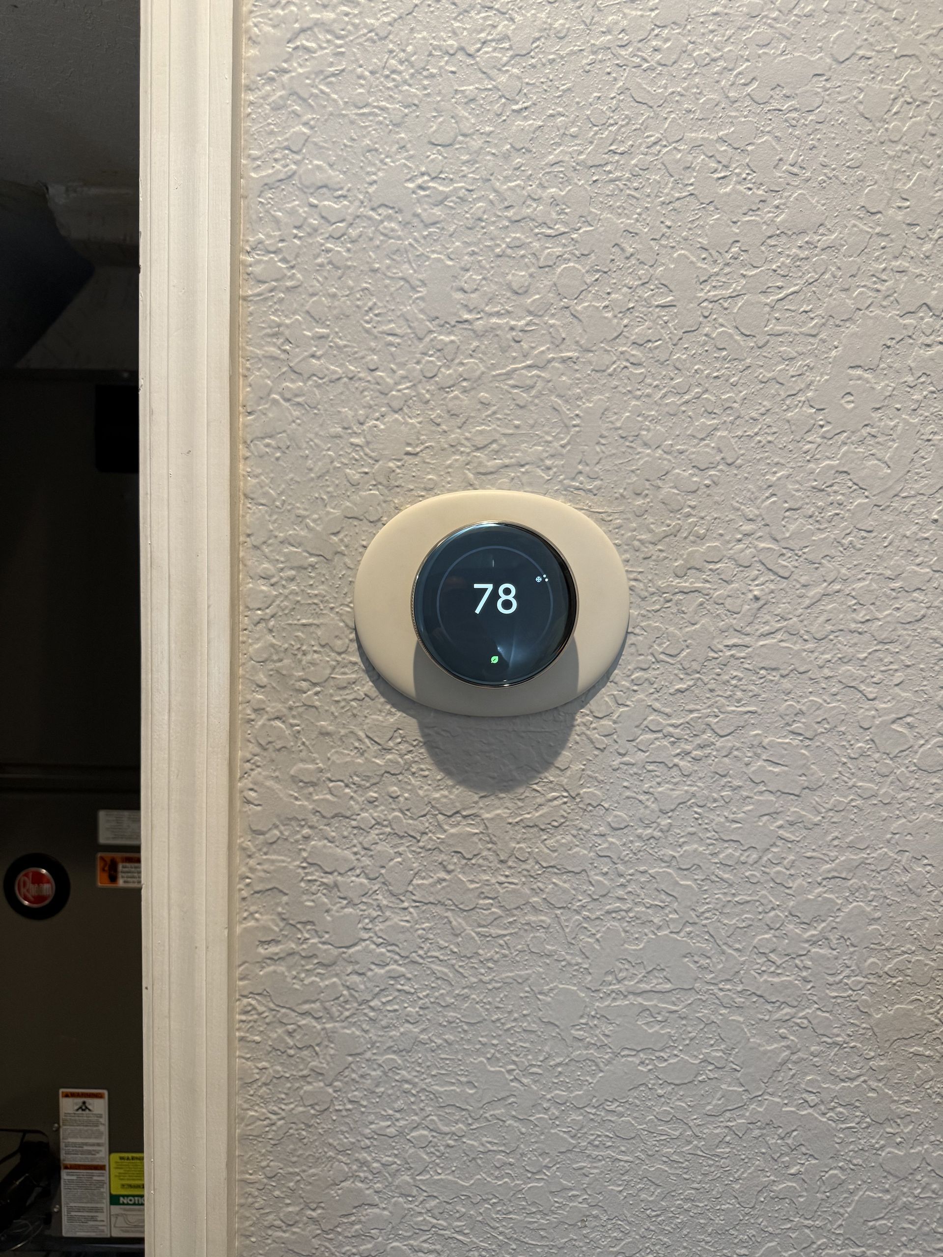A circular Nest smart thermostat with a black display showing 78 degrees, mounted on a textured beige wall.