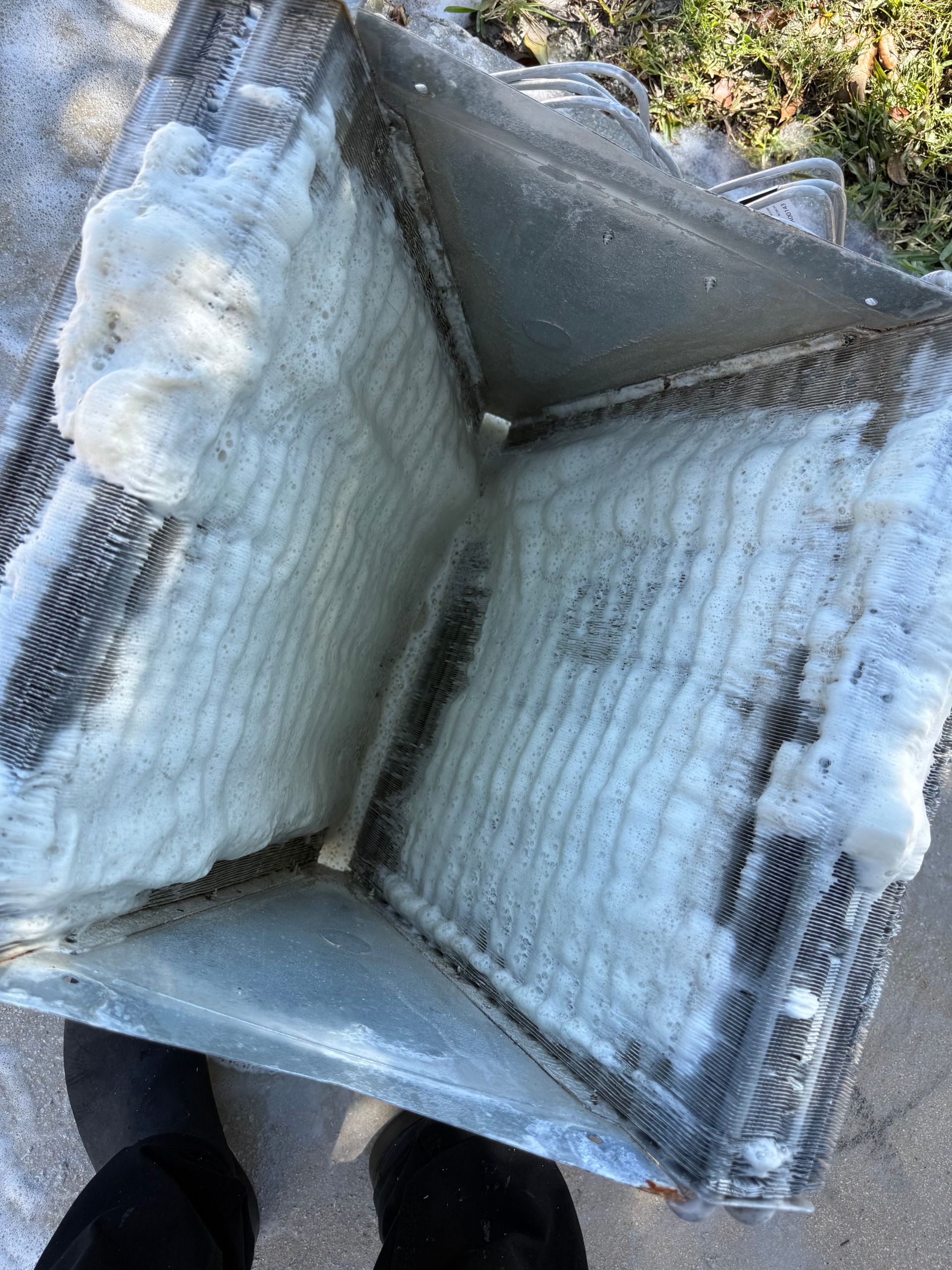 A residential air conditioning evaporator coil heavily coated in white ice, held outdoors above a concrete surface.