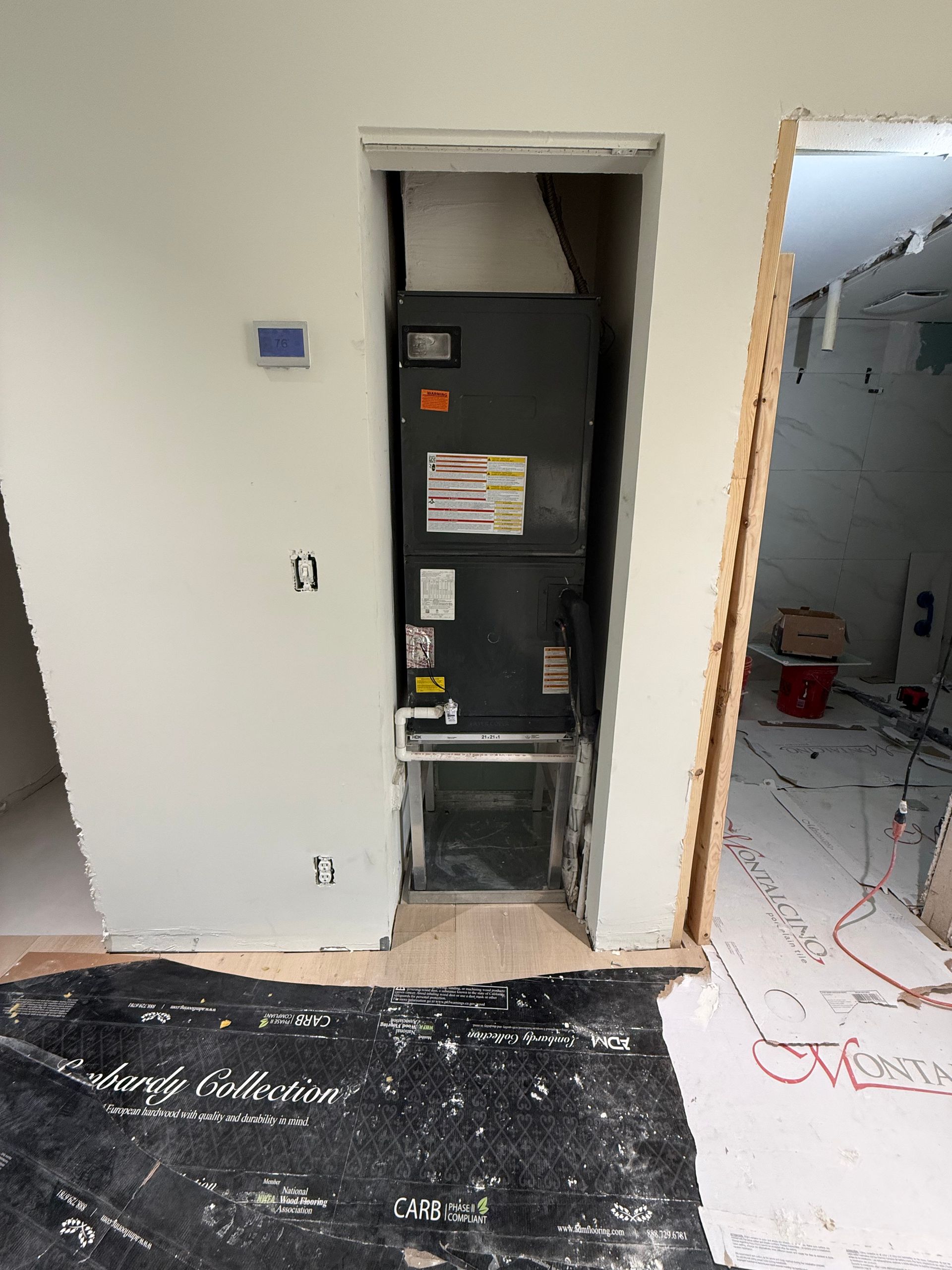 A black HVAC unit sits in a wall cutout within a room under renovation with exposed flooring and construction materials.
