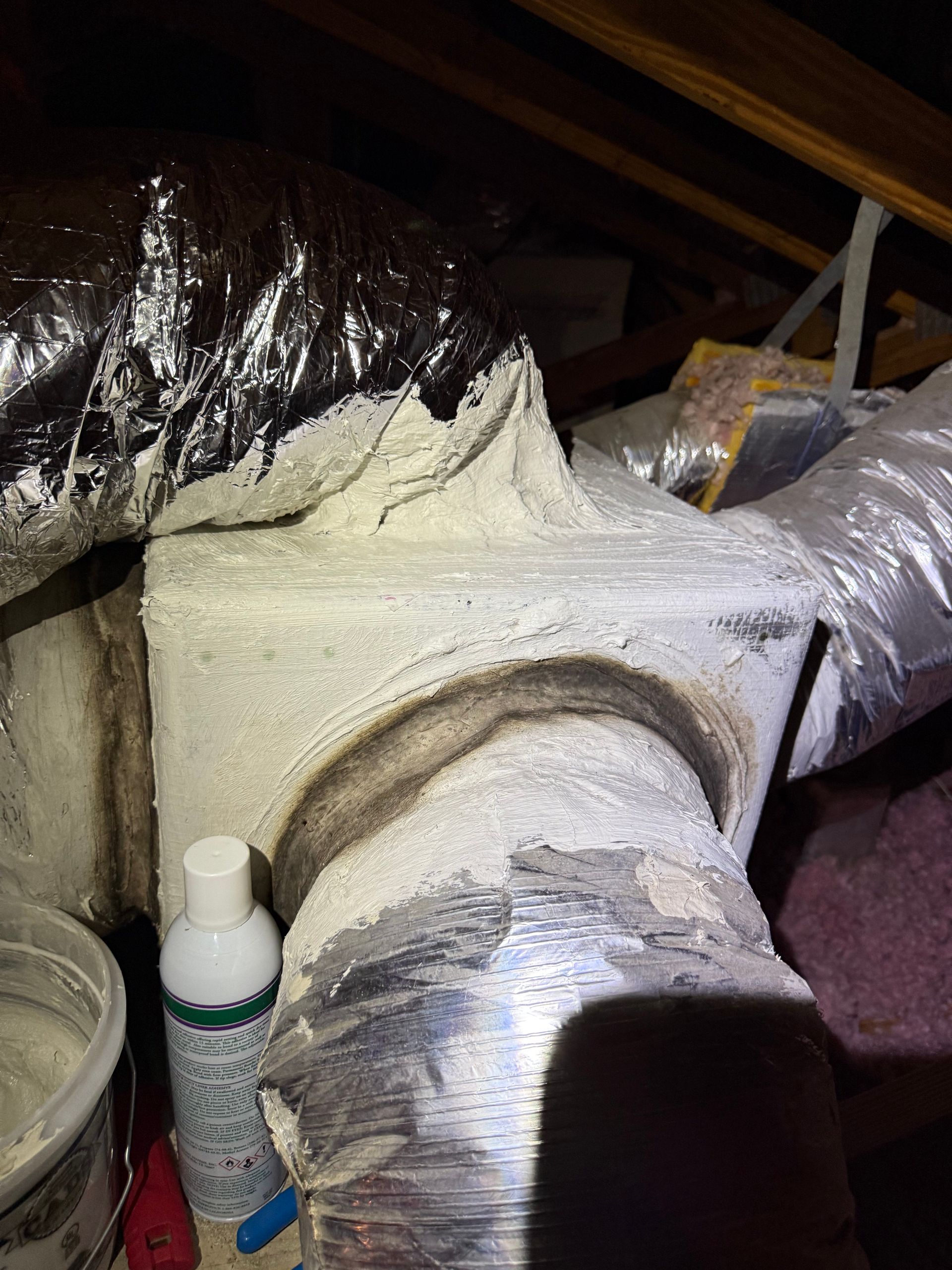 HVAC ductwork in an attic, coated in a thick, textured white sealant at the connections.