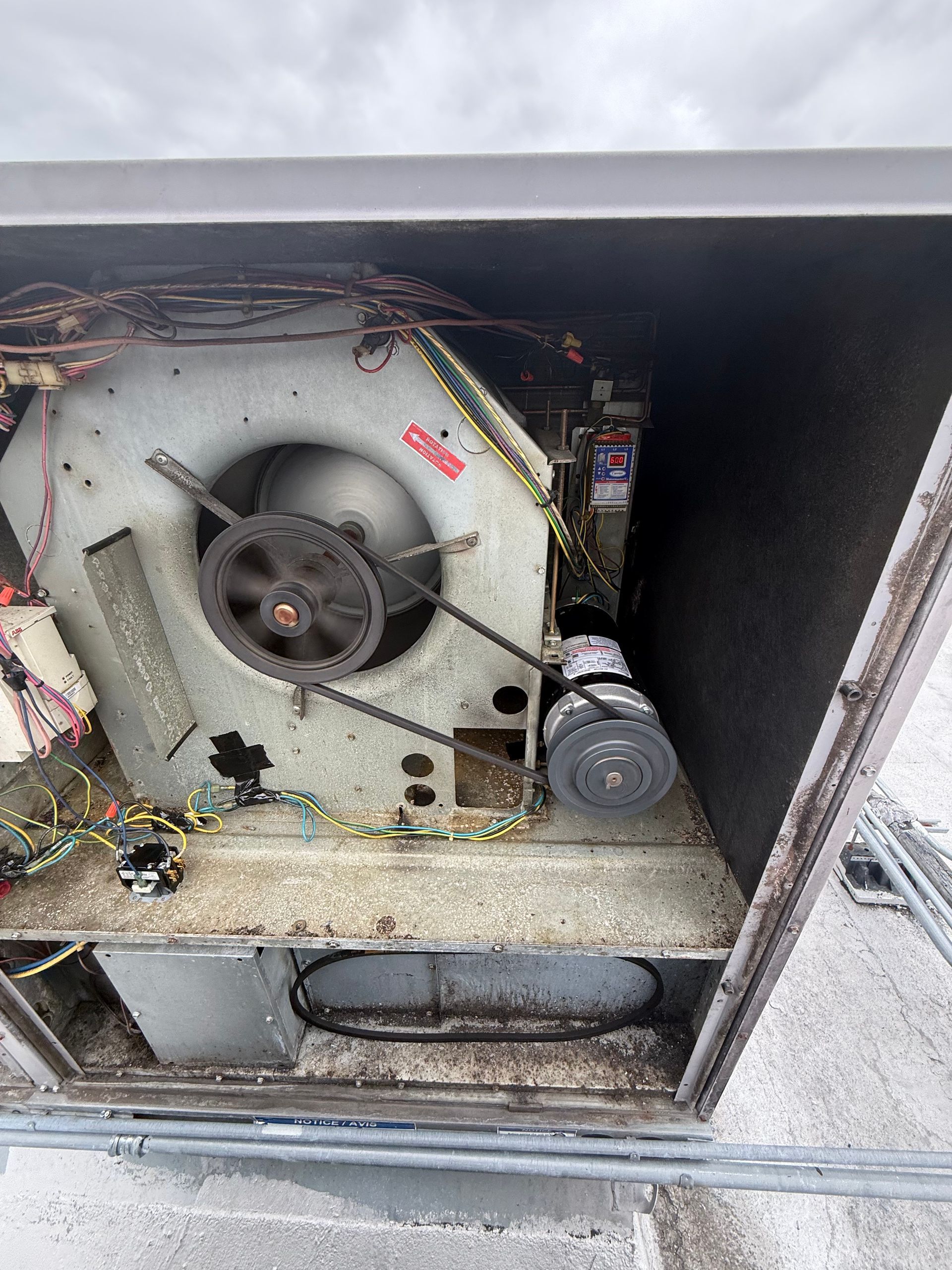 Interior of a rooftop HVAC unit showing a blower fan, a drive belt connected to a motor, and surrounding electrical wires.