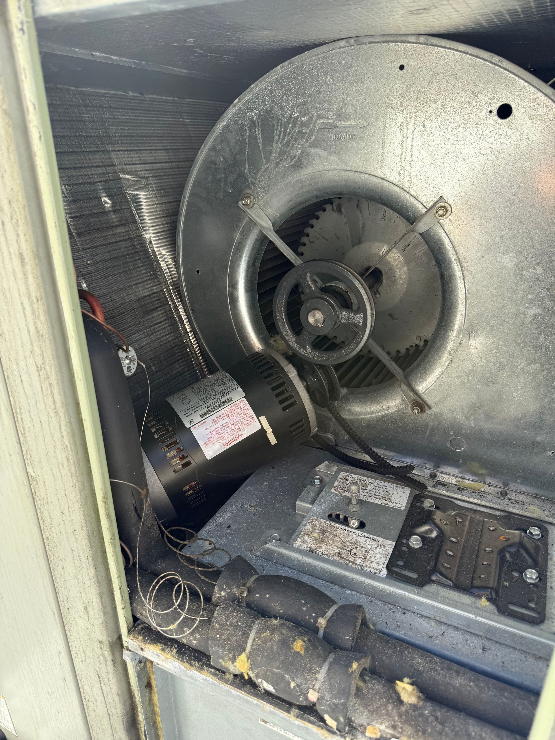 The interior compartment of an HVAC unit showing a blower motor attached to a metal fan assembly and insulated piping.
