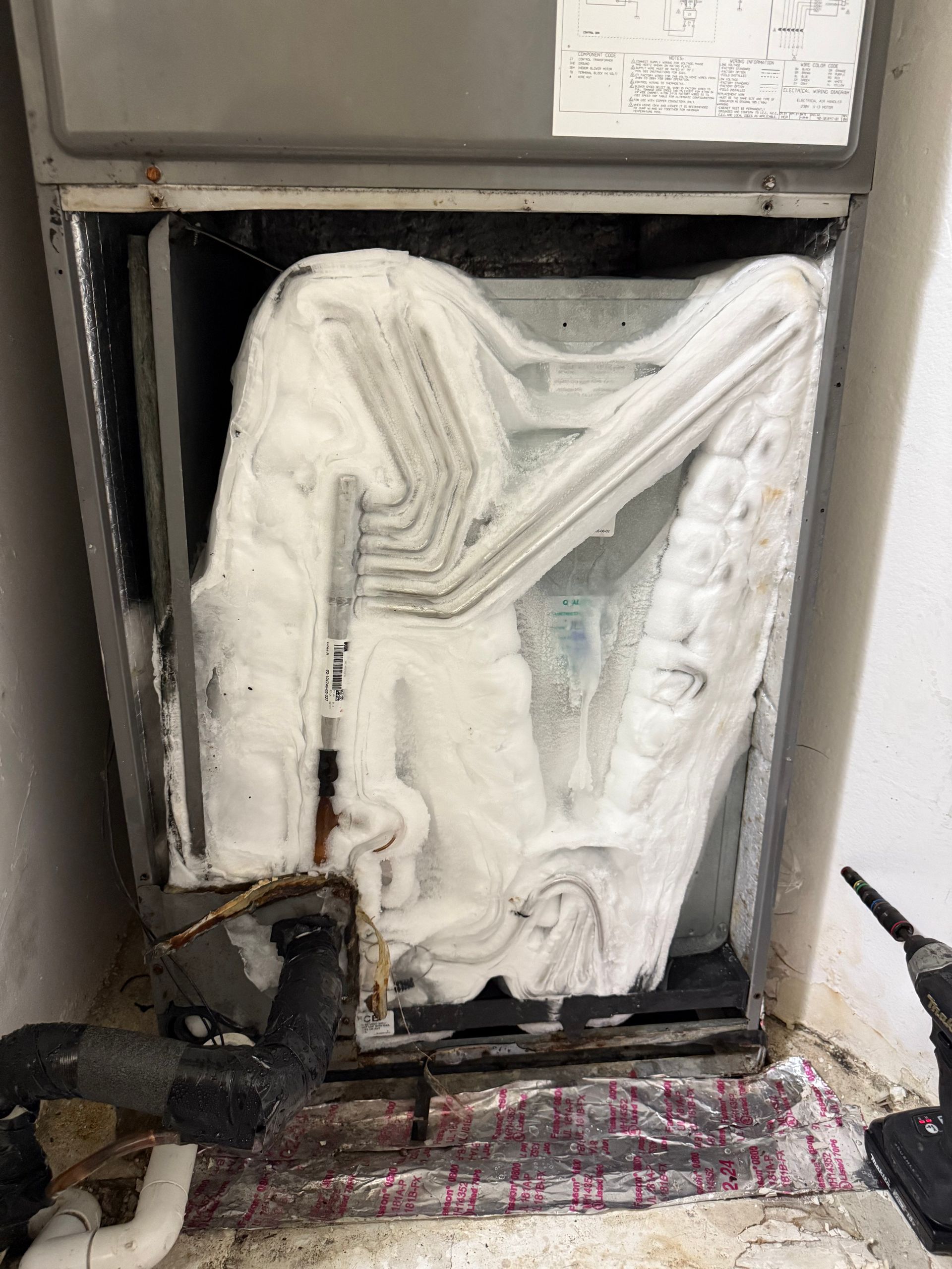 An HVAC evaporator coil inside a metal unit is heavily coated in a thick layer of white ice.