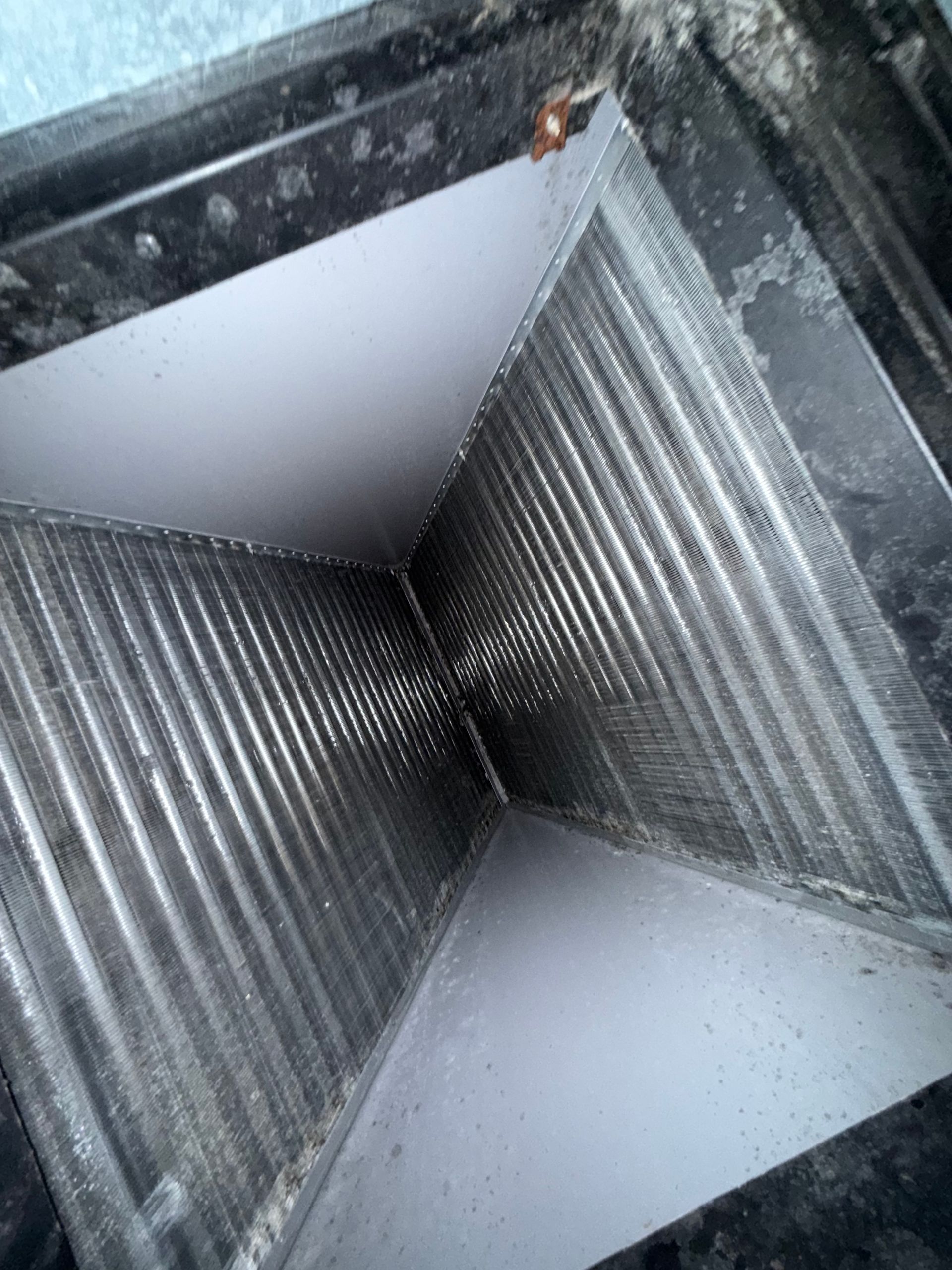 Interior view of an HVAC A-frame evaporator coil assembly with metal fins and drainage pans.