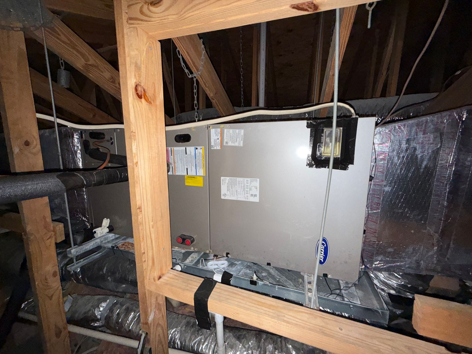 An HVAC air handler unit installed in an attic crawl space with visible ductwork and electrical wiring.