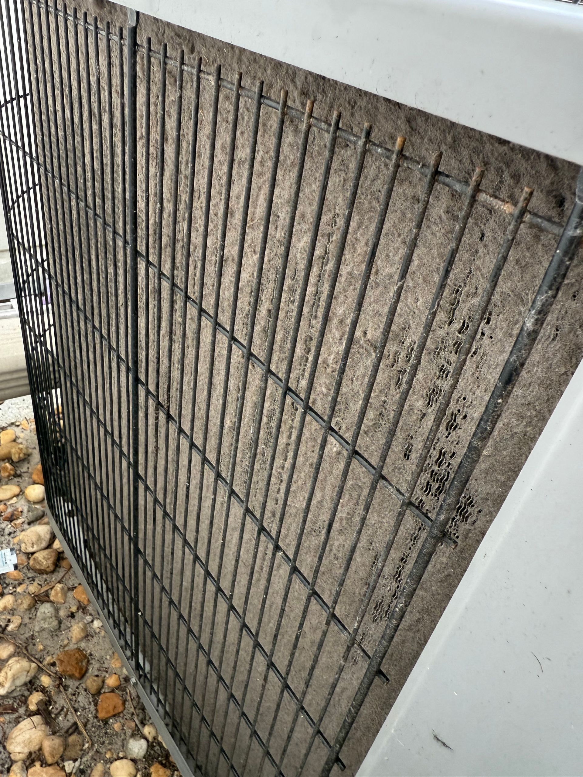 Close-up of a dirty, debris-clogged HVAC outdoor unit coil behind a black metal protective grate.