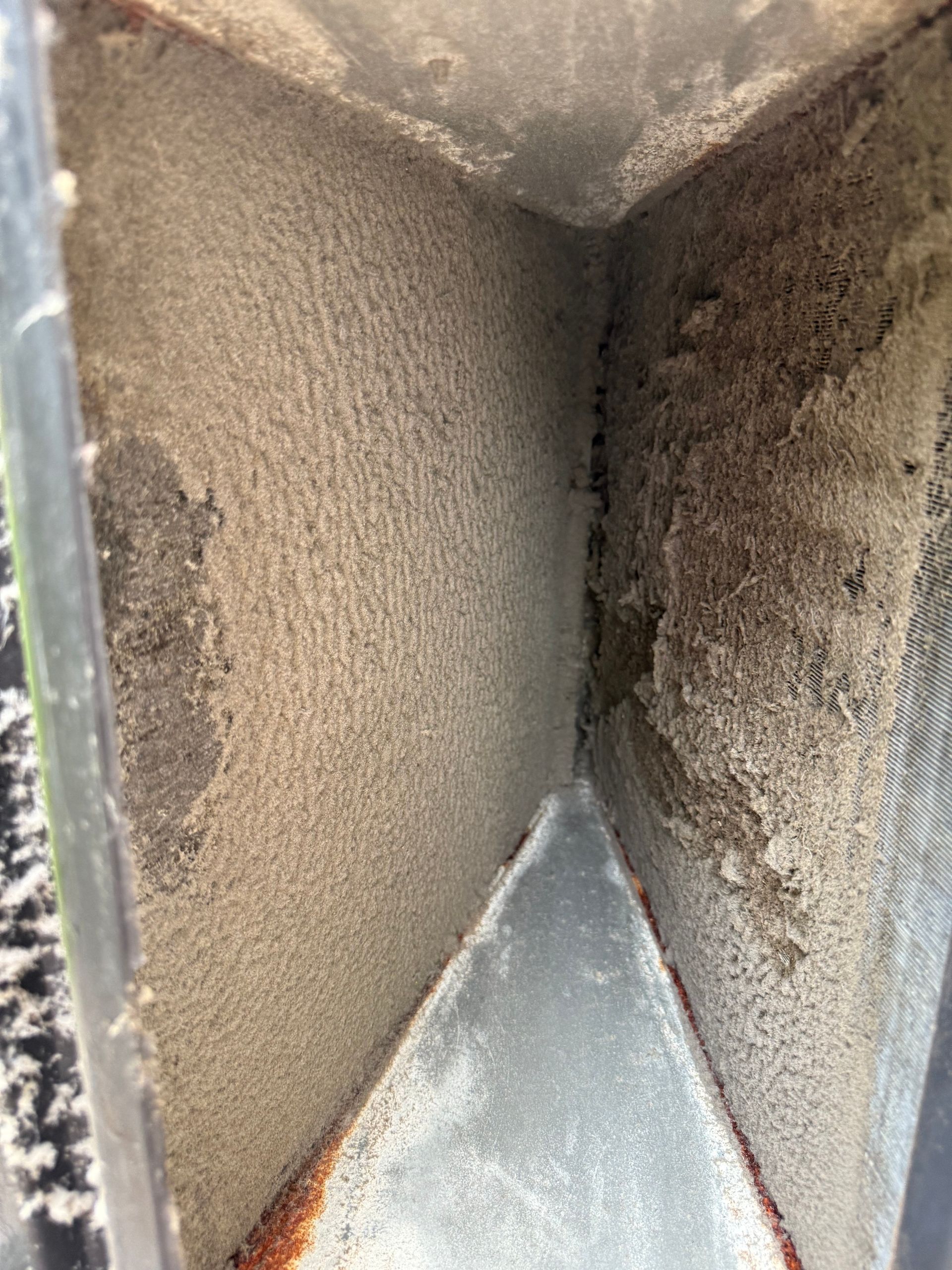 An HVAC evaporator coil caked with a thick layer of dust and debris, obstructing the metal fins.