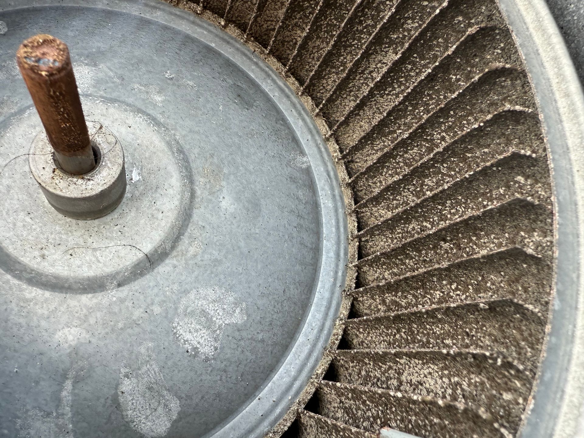 A top-down view of a circular HVAC blower fan heavily coated in thick, grey dust and debris on its blades.